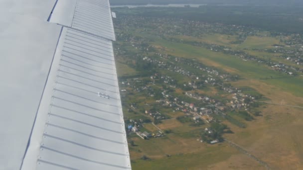 De witte vleugel van een passagiersvliegtuig tegen de top uitzicht op de natuur achtergrond van een prachtig blauw meer, vliegt over een vijver, groene bossen en kleine huizen en steden. Reisconcept — Stockvideo