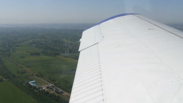 在白色机翼的背景下，从一架小型私人客机的窗口观看。房屋、绿林、田野、湖泊、河流尽收眼底 — 图库视频影像