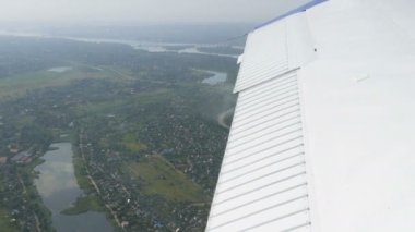 Küçük bir yolcu uçağının penceresinden beyaz bir kanada bakan manzara. Beyaz bir kanadın arka planına karşı doğa, nehir ve yeşil alanların üst görünümü