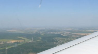 Yeşil ormanların, sarı tarlaların, küçük evlerin ve kasabaların üst manzarasına karşı bir yolcu uçağının beyaz kanadı. Seyahat kavramı