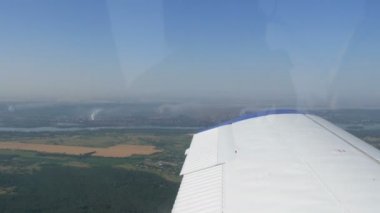 Küçük bir yolcu uçağının penceresinden beyaz bir kanadın arka planına bakın. Üst manzara yeşil alanlar ve rezervler