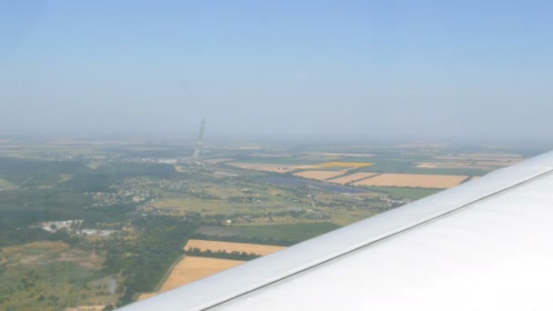 The white wing of a passenger plane against the top view of green forests, yellow fields and small houses and towns. Travel concept — Stock Footage The white wing of a passenger plane against the top view of green forests, yellow fields and small houses and towns. Travel concept Stock Video