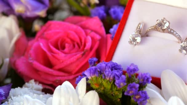 Nahaufnahme des Geschenks Geschenk rote Box mit einem Satz Verlobungsring und Ohrringe auf dem Hintergrund eines bunten schönen Blumenstrauß. Heiratsantrag, ein neues glückliches Leben. — Stockvideo