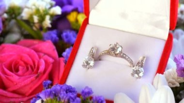 Çok renkli güzel bir buket çiçeğin arka planında nişan yüzüğü ve küpeleriyle hediye edilen kırmızı kutunun yakın görüntüsü. Evlilik teklifi, yeni mutlu bir hayat..