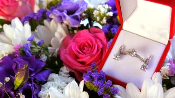 Top kilátás ajándék jelen piros doboz egy sor eljegyzési gyűrű és fülbevaló a háttérben egy sokszínű gyönyörű csokor virág. Házassági ajánlat, új boldog élet. — Stock videók