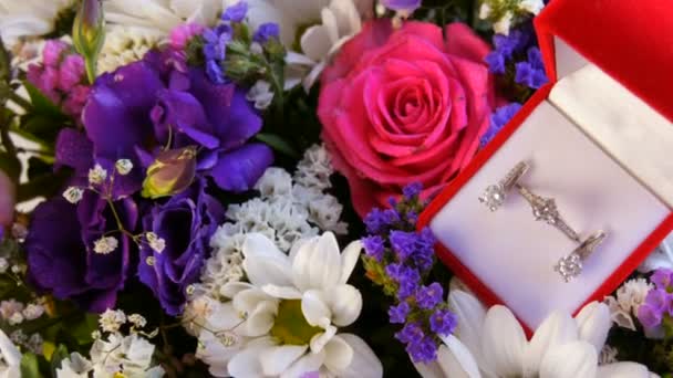 Top kilátás ajándék jelen piros doboz egy sor eljegyzési gyűrű és fülbevaló a háttérben egy sokszínű gyönyörű csokor virág. Házassági ajánlat, új boldog élet. — Stock videók