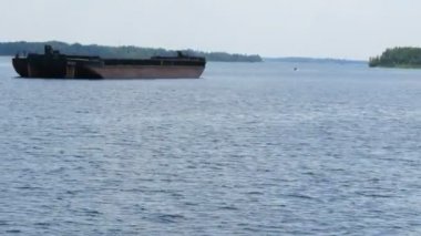 Nehir veya göl arasında terk edilmiş eski paslı bir mavnanın yanından geçiyor.