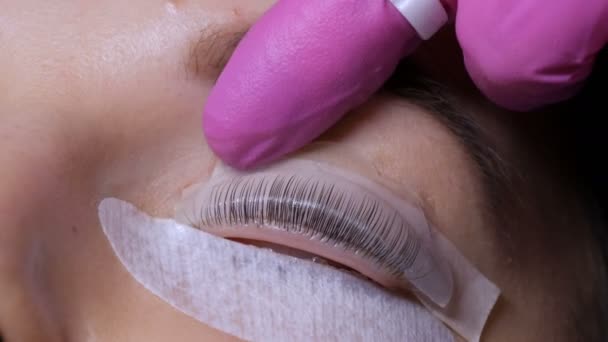 Gesicht eines jungen Mädchens vor einem modernen Wimpernkaschierungsverfahren in einem professionellen Schönheitssalon. Der Meister trägt vor dem Wimpernkräuseln Spezialkleber in rosa Gummihandschuhen auf — Stockvideo