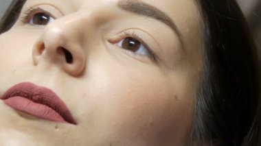 Kirpik kıvırma işleminden önce profesyonel bir güzellik salonunda modern kirpik kirpikleme prosedüründen önce genç bir kızın yüzünü kapatın. Siyah rujlu makyajsız bir kadın portresi.