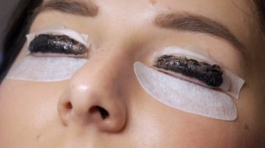 Profesyonel bir güzellik salonunda kirpik temizleme işlemi yapan genç bir kızın yüzü. Usta kirpik kıvırma işlemi sırasında kirpiklere özel bir fırçayla siyah boya sür