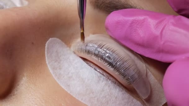 Gesicht eines jungen Mädchens vor einem modernen Wimpernkaschierungsverfahren in einem professionellen Schönheitssalon. Beim Wimpernkräuseln trägt der Meister eine Chemikalie mit einer speziellen Bürste auf. — Stockvideo