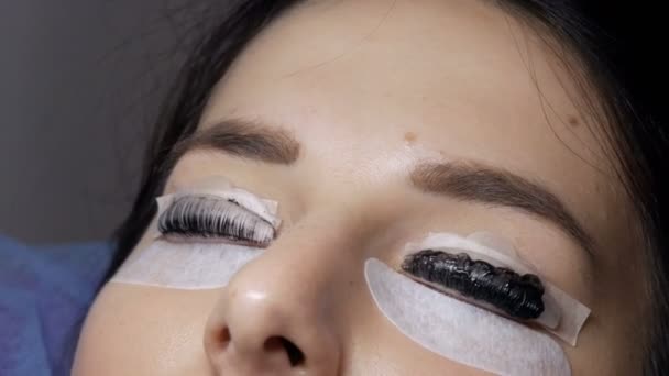 Face of young girl before eyelash lamination procedure in a professional beauty salon. The master washes off the black paint on the eyelashes during the eyelash curling procedure with a special brush — Stock Video