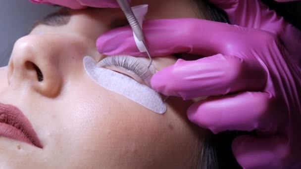 Gezicht van een jong meisje voor een moderne wimper lamineren procedure in een professionele schoonheidssalon. De master brengt speciale lijm aan voordat de wimper curling procedure in roze rubberen handschoenen close-up — Stockvideo