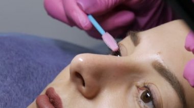 Profesyonel bir güzellik salonunda genç bir kızın modern kirpik kaplama prosedürünün yüzü. Usta kirpikleri özel bir fırçayla tarıyor. Kirpik kıvırma işlemi sırasında özel bir fırçayla.