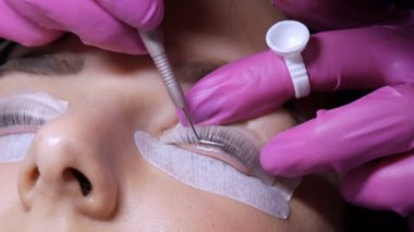 Profesyonel bir güzellik salonunda modern kirpik temizleme prosedüründen önce genç bir kızın yüzü. Pembe lastik eldivenlerle kirpik kıvırma prosedüründen önce usta özel yapıştırıcı uyguluyor.