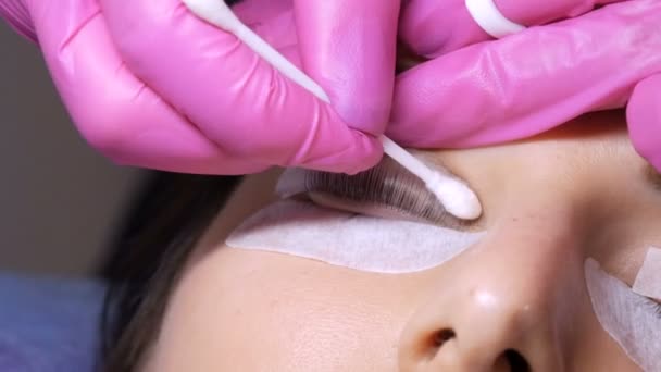 Gezicht van een jong meisje voor een moderne wimper lamineren procedure in een professionele schoonheidssalon. De master wast de speciale lijm af met een wattenstaafje voor de wimperkrulprocedure — Stockvideo