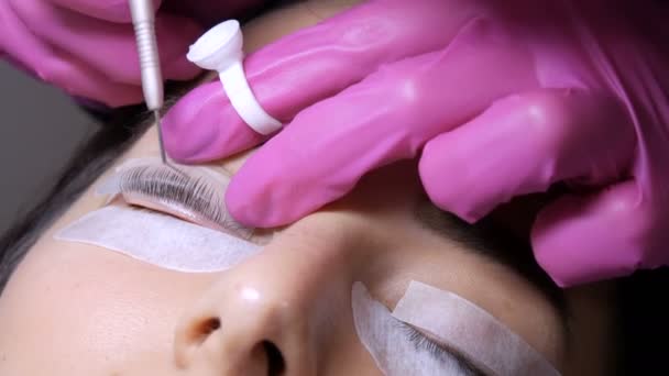 Face of a young girl before a modern eyelash lamination procedure in a professional beauty salon. The master applies special glue before the eyelash curling procedure in pink rubber gloves close up — Stock Video