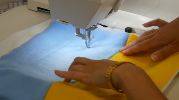 Игла швейной машинки для вышивки делает орнамент на куске синей и желтой ткани. Женские руки двигают ткань и подножие иглы — стоковое видео