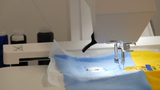 La aguja de la máquina de coser para bordar hace un adorno en un pedazo de tela azul y amarilla. Máquina de coser especial para bordar en el trabajo. Máquina de coser programable — Vídeo de stock