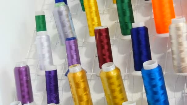 Una fila de hilos multicolores diferentes para una máquina de coser y overlock en un taller de costura o atelier. Filas carretes de hilo de diferentes colores en la máquina de coser industrial. — Vídeos de Stock