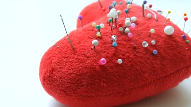 Pin cuscino sotto forma di un cuore rosso morbido in cui molti spilli e aghi per il ricamo e il cucito sono bloccati in un laboratorio di cucito o atelier — Video Stock