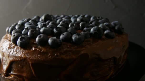 Nahaufnahme von Brownie-Schokoladenkuchen mit Kakao-Zuckerguss und Blaubeeren auf stilvollem schwarzem Hintergrund in leisen Tönen — Stockvideo