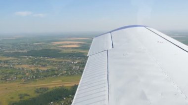 Yeşil ormanların, sarı tarlaların, küçük evlerin ve kasabaların üst manzarasına karşı bir yolcu uçağının beyaz kanadı. Seyahat kavramı