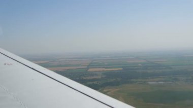 Küçük bir yolcu uçağının penceresinden beyaz bir kanadın arka planına bakın. Üst manzara yeşil alanlar ve rezervler