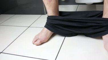 Banyoda tuvalette oturan bir adamın bacakları. Dışkılama işlemi. Evdeki tuvalet. Sabahları sağlıklı bağırsak hareketleri.