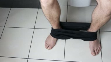 Banyoda tuvalette oturan bir adamın bacakları. Dışkılama işlemi. Evdeki tuvalet. Sabahları sağlıklı bağırsak hareketleri.