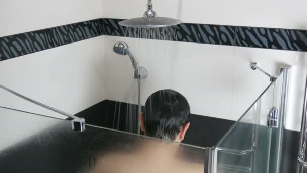 Ένας νεαρός πλένεται κάτω από το ντους. Πλένεις τα μαλλιά σου κάτω από τρεχούμενο νερό στο ντους το πρωί ή το βράδυ. Μοντέρνο μοντέρνο εσωτερικό μπάνιο — Αρχείο Βίντεο