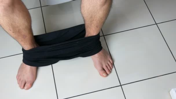 Πόδια ενός άντρα που κάθεται στην τουαλέτα στο μπάνιο. Διαδικασία αφόδευσης. Τουαλέτα στο σπίτι. Υγιείς κινήσεις του εντέρου το πρωί — Αρχείο Βίντεο