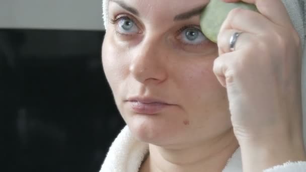 Piękna kobieta z ręcznikiem na głowie robi masaż jadeitowym kamieniem Skrobak do twarzy z gwaszem Masaż twarzy w łazience. Chińskie narzędzia piękności. Masaż limfatyczny skóry przed starzeniem się zmarszczek — Wideo stockowe