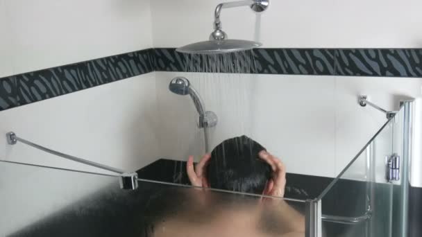 Un joven se está lavando bajo la ducha. Lavarse el cabello con agua corriente en la ducha por la mañana o por la noche. Interior de baño moderno de moda — Vídeo de stock