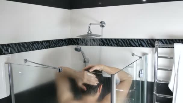 Genç bir adam duşun altında kendini yıkıyor. Sabah ya da akşam duşta saçlarını akan suyun altında yıkamak. Modern banyo iç mimarisi. — Stok video