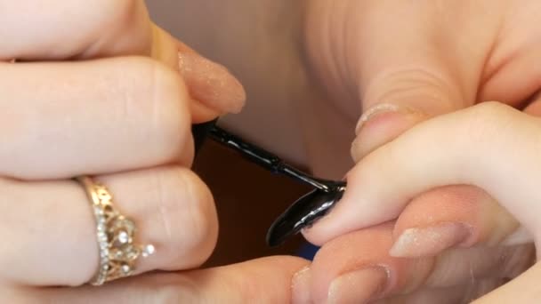 En manikyrist målar en lång förlängd nagel för en klient med svart nagellack — Stockvideo