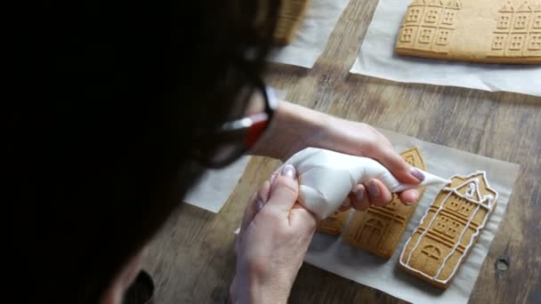 Brun pepperkakeglasur. Kvinnelige kokker dekorerer med hvit sukkerglasur og konditorposer. Et pepperkakehus på kjøkkenet. Nyårstradisjoner – stockvideo