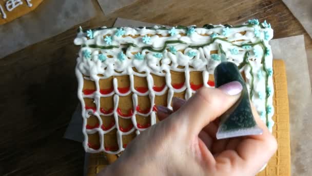 Пряничная глазурь. Шеф-повара женские руки украшают зеленой сахарной глазурью и кондитерской сумкой пряничного домика на домашней кухне. Новогодние традиции — стоковое видео