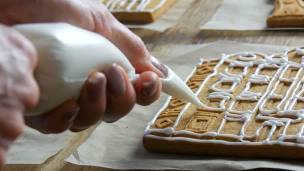 Glassa di pan di zenzero marrone. Le chef donne decorano con glassa di zucchero bianco e sacchetto di pasticceria una casa di Natale di pan di zenzero nella cucina di casa. Le tradizioni di anno nuovo — Video Stock