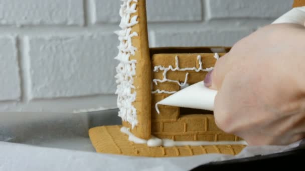 妇女装饰姜饼屋与糕点袋白糖甜糖霜，手放在白砖背景。做饭，烘焙自制姜饼屋的圣诞假期。新年传统 — 图库视频影像