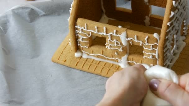여자들은 흰 벽돌로 만든 배경 위에 흰 설탕을 달아 만든 과자 가방으로 진저브레드 하우스를 장식한다. 요리, 크리스마스 휴일에 집에서 만든 생강 빵 집 요리. 새해 전통 — 비디오