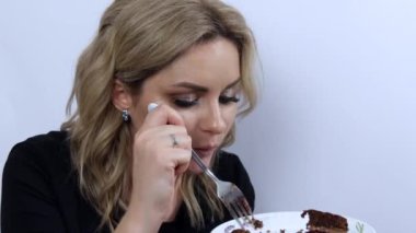 Beyaz arka planda çikolatalı kek yiyen güzel bir model. Güzel dumanlı göz makyajı ve siyah gece elbisesi olan genç bir kız.