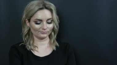 Parlak makyajlı, dumanlı gözlü ve siyah elbiseli güzel bir kadın siyah arka planda düşünceli görünüyor. Stüdyoda kız model