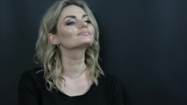 Parlak makyajlı, dumanlı gözlü ve siyah elbiseli güzel bir kadın siyah arka planda düşünceli görünüyor. Stüdyoda kız model