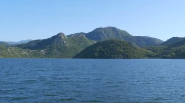 Mavi nehir yeşil vadiden uzak dağlara doğru akıyor. Karadağ milli parkındaki Crnojevica nehrinin kıvrımları ve kıvrımları, Skadar Gölü 'ne giden tepelerin arasında bataklıktan geçiyor.