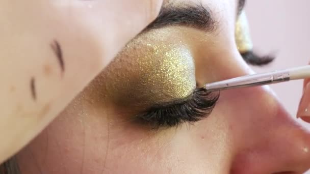 Kuas eyeliner hitam halus diterapkan pada riasan malam dalam tampilan close-up nada emas — Stok Video