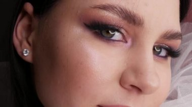 Güzel bir modelin portresi. Beyaz bir duvaklı dumanlı gözlerle poz veriyor. Uzun kirpik uzantıları ve yumuşak pembe tonlarda göz makyajı.