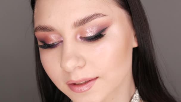 Retrato de una hermosa joven modelo en elegante noche maquillaje ojos ahumados mira a la cámara y posando. Ojos de cerca. Extensiones de pestañas largas y maquillaje de ojos en tonos rosados suaves — Vídeos de Stock