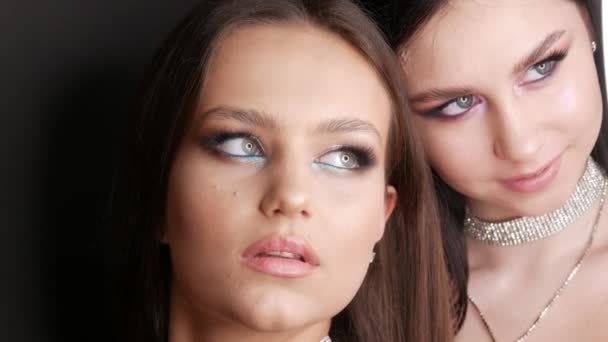 Retrato de dos hermosa joven modelo en elegante noche componen ojos ahumados mira a la cámara y posando. Ojos de cerca. Extensiones de pestañas largas y maquillaje de ojos y collar de diamantes de imitación — Vídeo de stock