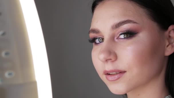 Retrato de una hermosa joven modelo en elegante noche maquillaje ojos ahumados mira a la cámara y posando. Ojos de cerca. Extensiones de pestañas largas y maquillaje de ojos en tonos rosados suaves — Vídeos de Stock